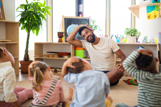 Teacher practicing emotional wellness with his students by doing yoga in classroom